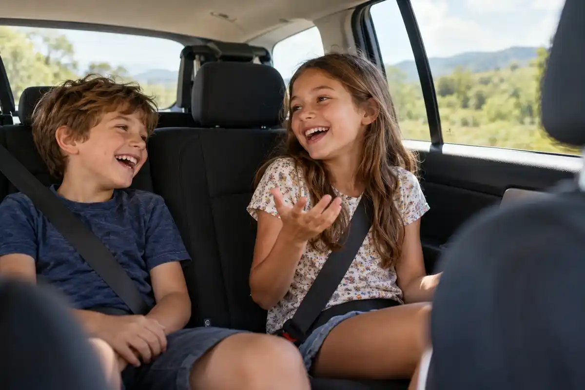 Two siblings laughing in the back seat of the car while playing would you rather on a road trip